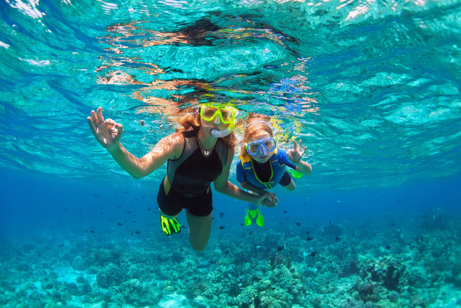 Mother, kid in snorkeling mask dive underwater with tropical fishes