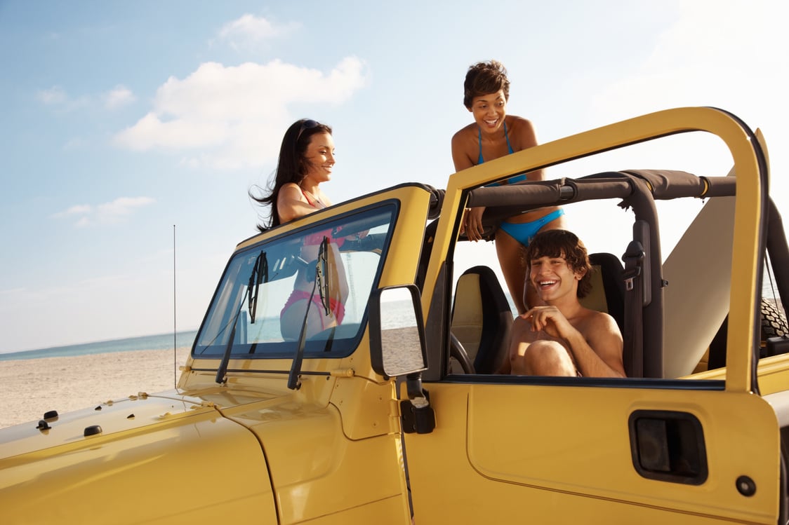 Three young friends in jeep enjoying their vacation on beach